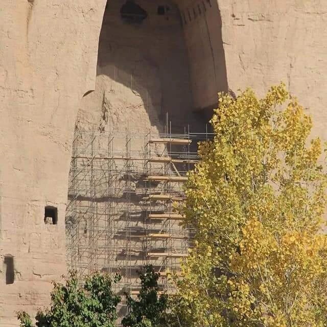 Leere Nische der zerstörten Buddha-Statuen von Bamiyan mit Gerüst zur Konservierung, herbstlich gefärbter Baum im Vordergrund